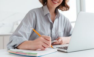Young girl smiling taking notes by hand and on computer