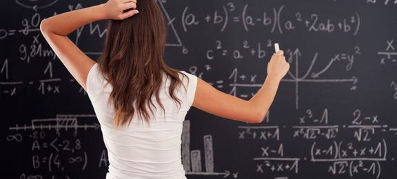 Молода жінка дивиться на завдання з алгебри та початків аналізу, написане на шкільній дошці