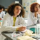 Happy teenage boy in labcoat looking at teacher of natural sciences