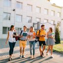 Five students walking around with books on university campus 