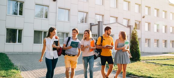 Five students walking around with books on university campus 